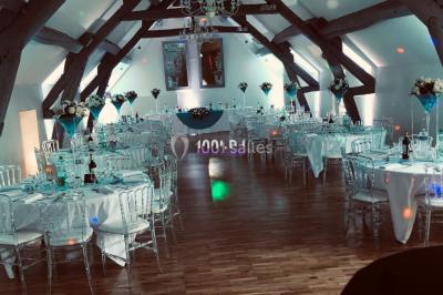 Salle de réception décorée avec des tables rondes éclairées en bleu, nappes blanches et bougies allumées.