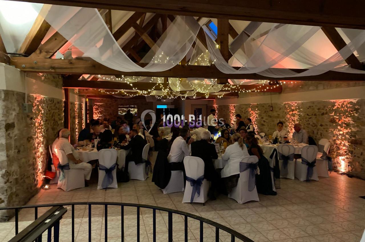 Salle de réception décorée avec des guirlandes lumineuses, des invités assis à des tables rondes lors d'un événement.
