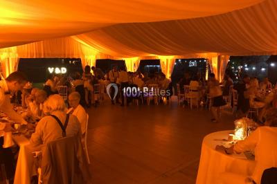 Salle de réception décorée avec des tables rondes éclairées en bleu, nappes blanches et bougies allumées.
