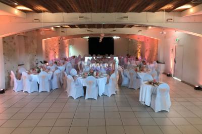 Salle de réception décorée avec des tables rondes éclairées en bleu, nappes blanches et bougies allumées.