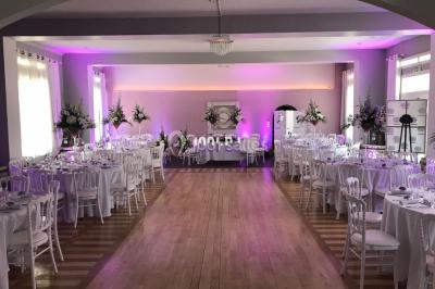 Salle de réception décorée avec des tables rondes éclairées en bleu, nappes blanches et bougies allumées.