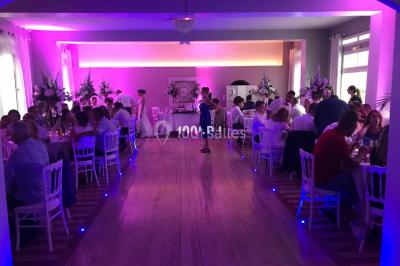 Salle de réception décorée avec des tables rondes éclairées en bleu, nappes blanches et bougies allumées.
