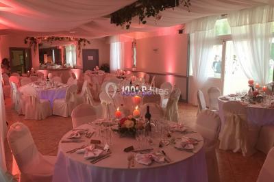 Salle de réception décorée avec des tables rondes éclairées en bleu, nappes blanches et bougies allumées.