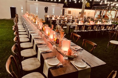 Table en bois dressée pour un repas, avec assiettes blanches, verres et décorations florales dans un cadre extérieur.
