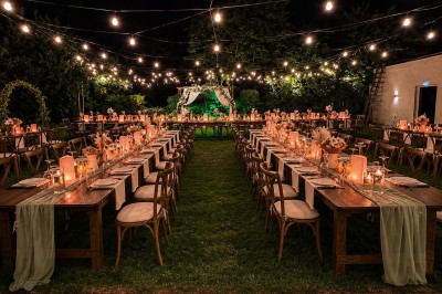 Table en bois dressée pour un repas, avec assiettes blanches, verres et décorations florales dans un cadre extérieur.