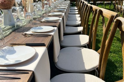Table en bois dressée pour un repas, avec assiettes blanches, verres et décorations florales dans un cadre extérieur.