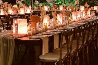 Table en bois dressée pour un repas, avec assiettes blanches, verres et décorations florales dans un cadre extérieur.