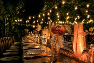 Table en bois dressée pour un repas, avec assiettes blanches, verres et décorations florales dans un cadre extérieur.