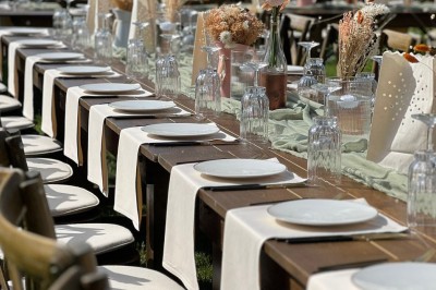 Table en bois dressée pour un repas, avec assiettes blanches, verres et décorations florales dans un cadre extérieur.