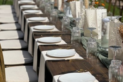Table en bois dressée pour un repas, avec assiettes blanches, verres et décorations florales dans un cadre extérieur.