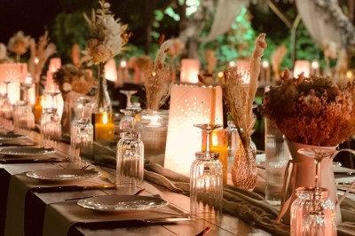 Table en bois dressée pour un repas, avec assiettes blanches, verres et décorations florales dans un cadre extérieur.
