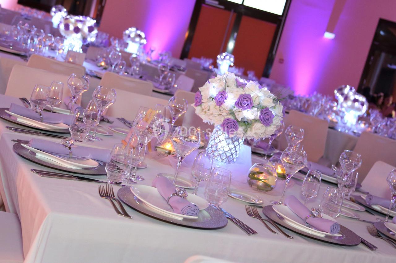 Tables élégamment dressées pour un événement, avec nappes blanches, décorations florales violettes et éclairage tamisé.