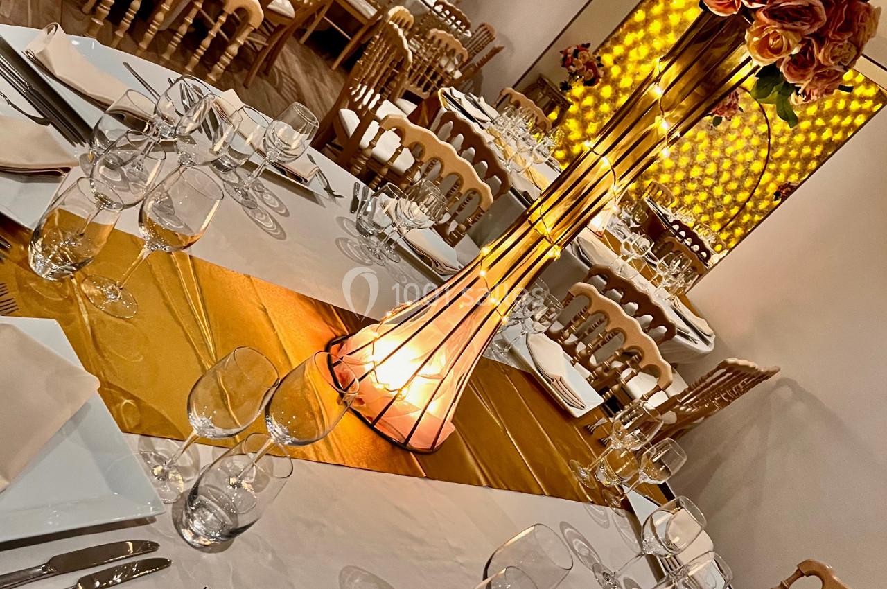 Salle de réception décorée avec des tables rondes, nappes blanches, centres de table fleuris et éclairage chaleureux.