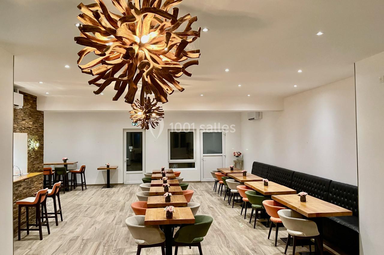 Salle de restaurant moderne avec tables alignées, chaises colorées et grand luminaire en bois sculpté au plafond.
