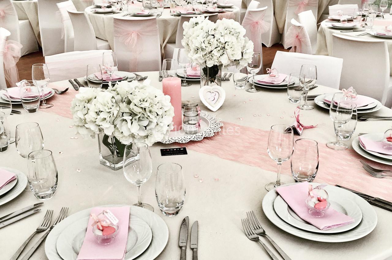 Tables élégamment dressées pour un événement, décorées de nappes blanches, fleurs blanches et accents roses.