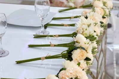 Arrangement floral blanc et rose sur une table dorée, avec un fond de rideaux roses et des décorations florales.
