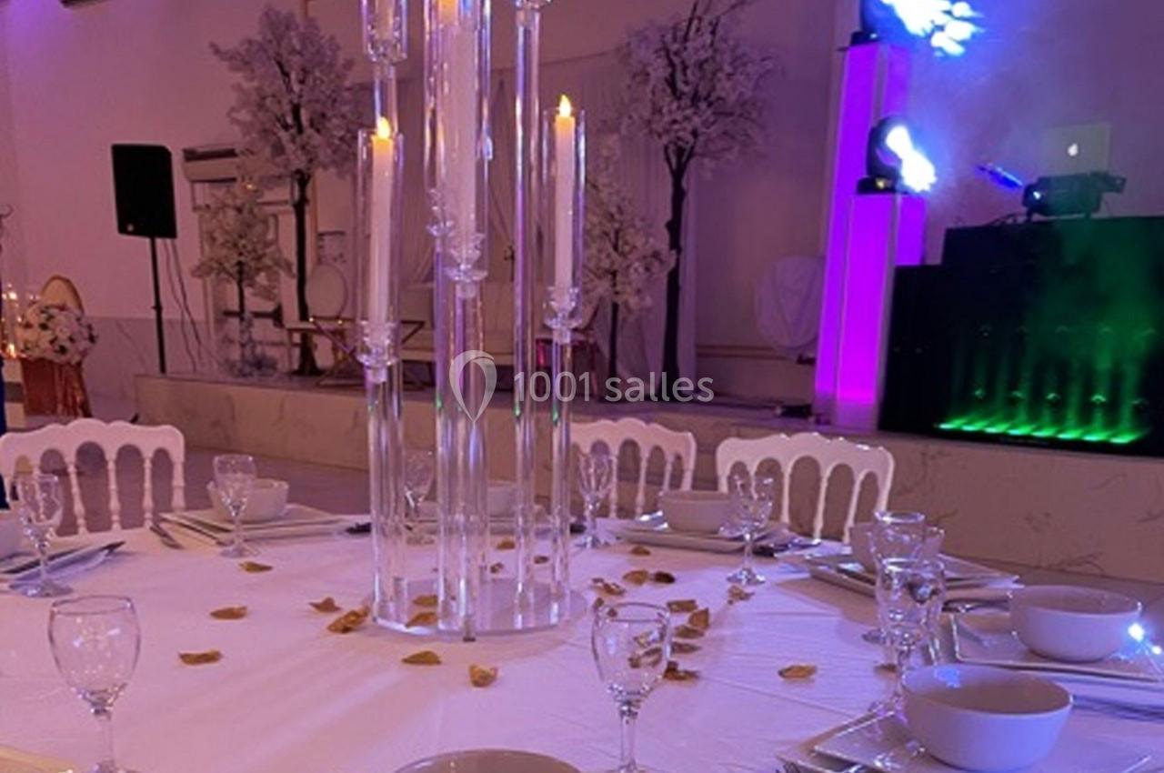 Table de réception élégamment dressée avec chandeliers en verre, pétales dorés et éclairage d'ambiance coloré.