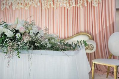 Arrangement floral blanc et rose sur une table dorée, avec un fond de rideaux roses et des décorations florales.