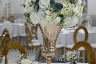 Arrangement floral blanc et rose sur une table dorée, avec un fond de rideaux roses et des décorations florales.