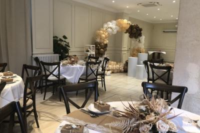 Salle décorée pour un événement, avec des tables rondes dressées, ornées de centres de table naturels et cadeaux.