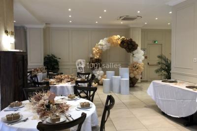 Salle décorée pour un événement, avec des tables rondes dressées, ornées de centres de table naturels et cadeaux.