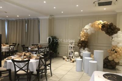 Salle décorée pour un événement, avec des tables rondes dressées, ornées de centres de table naturels et cadeaux.