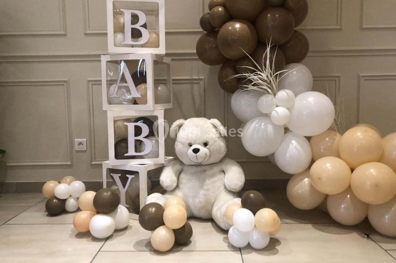 Décoration avec cubes ’BABY’, ours en peluche blanc et ballons beige, marron et blanc dans un intérieur lumineux.