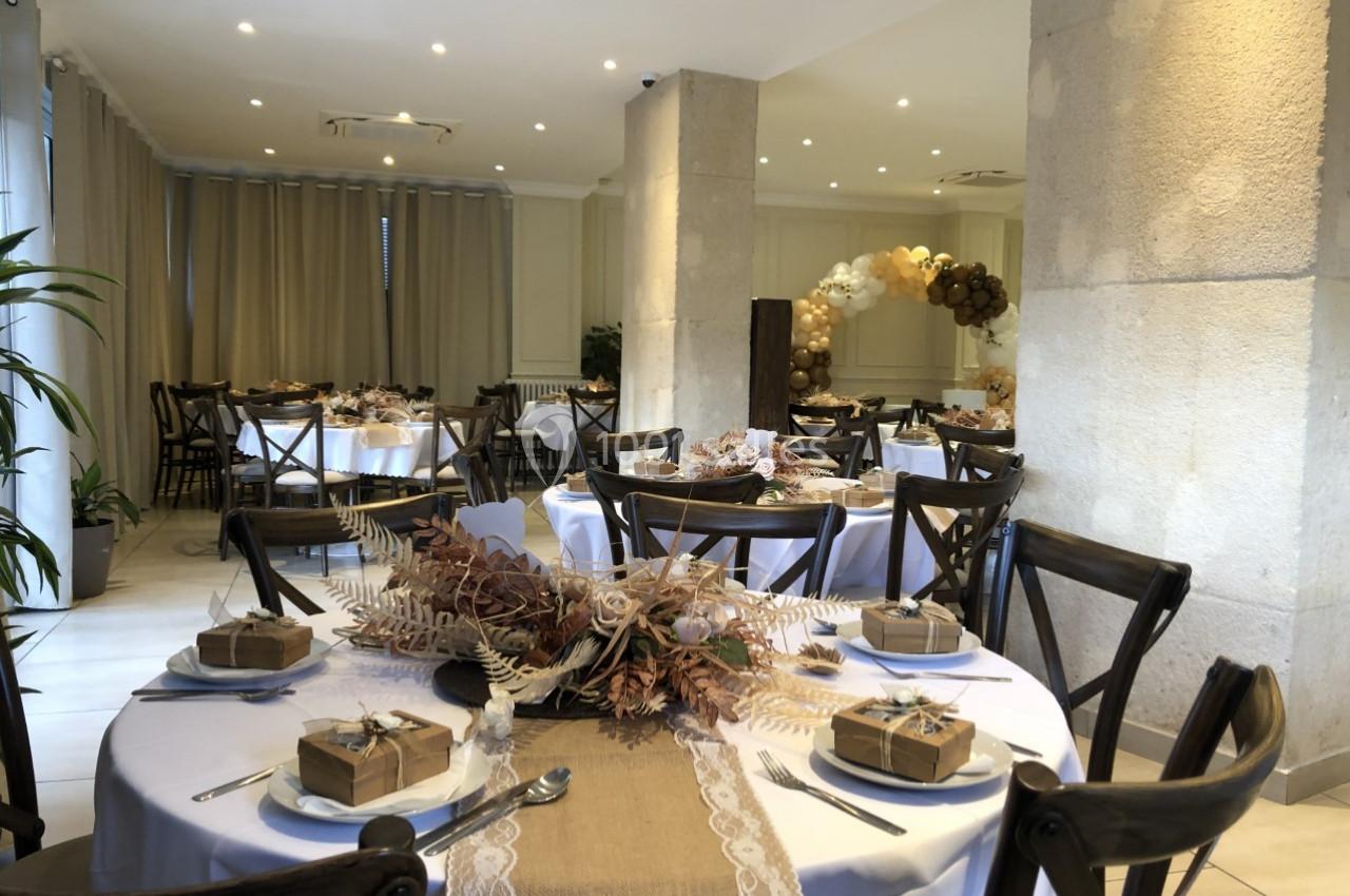 Salle de réception décorée avec des tables rondes, nappes blanches, centres de table floraux et cadeaux emballés.