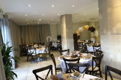 Salle décorée pour un événement, avec des tables rondes dressées, ornées de centres de table naturels et cadeaux.