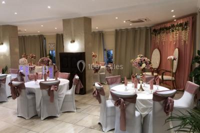 Salle décorée pour un événement, avec des tables rondes dressées, ornées de centres de table naturels et cadeaux.