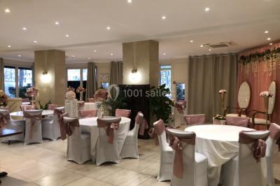 Salle décorée pour un événement, avec des tables rondes dressées, ornées de centres de table naturels et cadeaux.