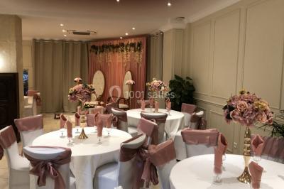 Salle décorée pour un événement, avec des tables rondes dressées, ornées de centres de table naturels et cadeaux.