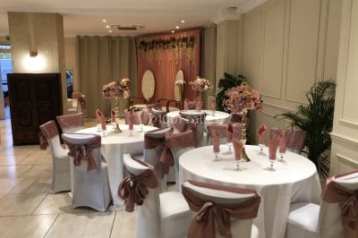 Salle décorée pour un événement, avec des tables rondes dressées, ornées de centres de table naturels et cadeaux.