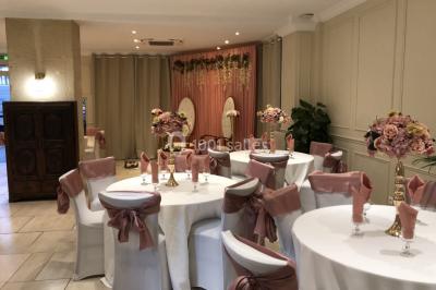 Salle décorée pour un événement, avec des tables rondes dressées, ornées de centres de table naturels et cadeaux.