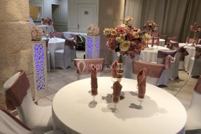 Salle décorée pour un événement, avec des tables rondes dressées, ornées de centres de table naturels et cadeaux.