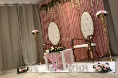 Salle décorée pour un événement, avec des tables rondes dressées, ornées de centres de table naturels et cadeaux.