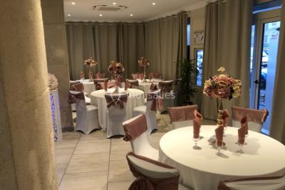 Salle décorée pour un événement, avec des tables rondes dressées, ornées de centres de table naturels et cadeaux.