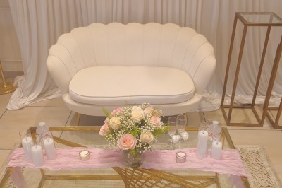Table ronde élégamment dressée avec nappes blanches, serviettes roses pliées, vaisselle et bouquet de fleurs au centre.
