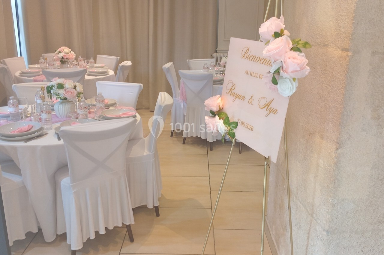 Salle de réception décorée pour un mariage avec des tables dressées et un panneau de bienvenue orné de fleurs.