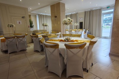 Table ronde élégamment dressée avec nappes blanches, serviettes roses pliées, vaisselle et bouquet de fleurs au centre.
