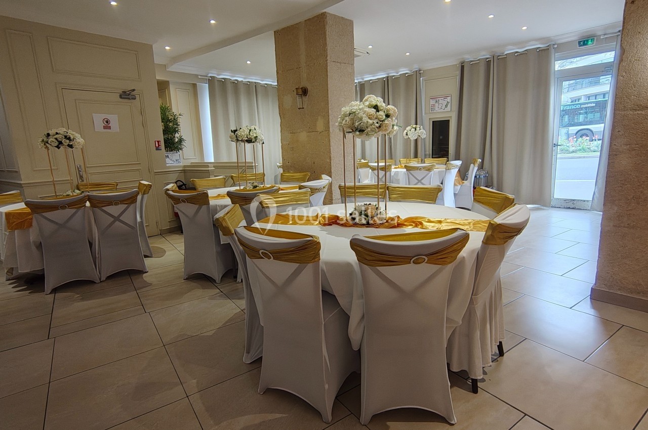 Salle de réception décorée avec des tables rondes, nappes blanches, chaises couvertes et centres de table floraux.