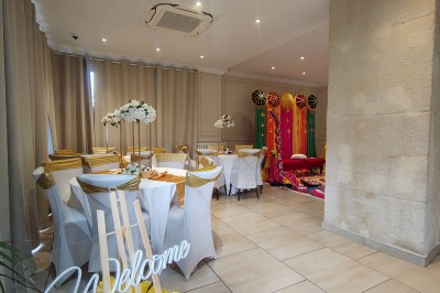 Table ronde élégamment dressée avec nappes blanches, serviettes roses pliées, vaisselle et bouquet de fleurs au centre.