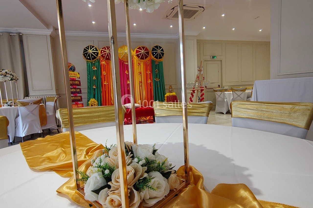 Salle décorée pour un événement avec des chaises dorées, une table ornée de fleurs et un fond coloré.