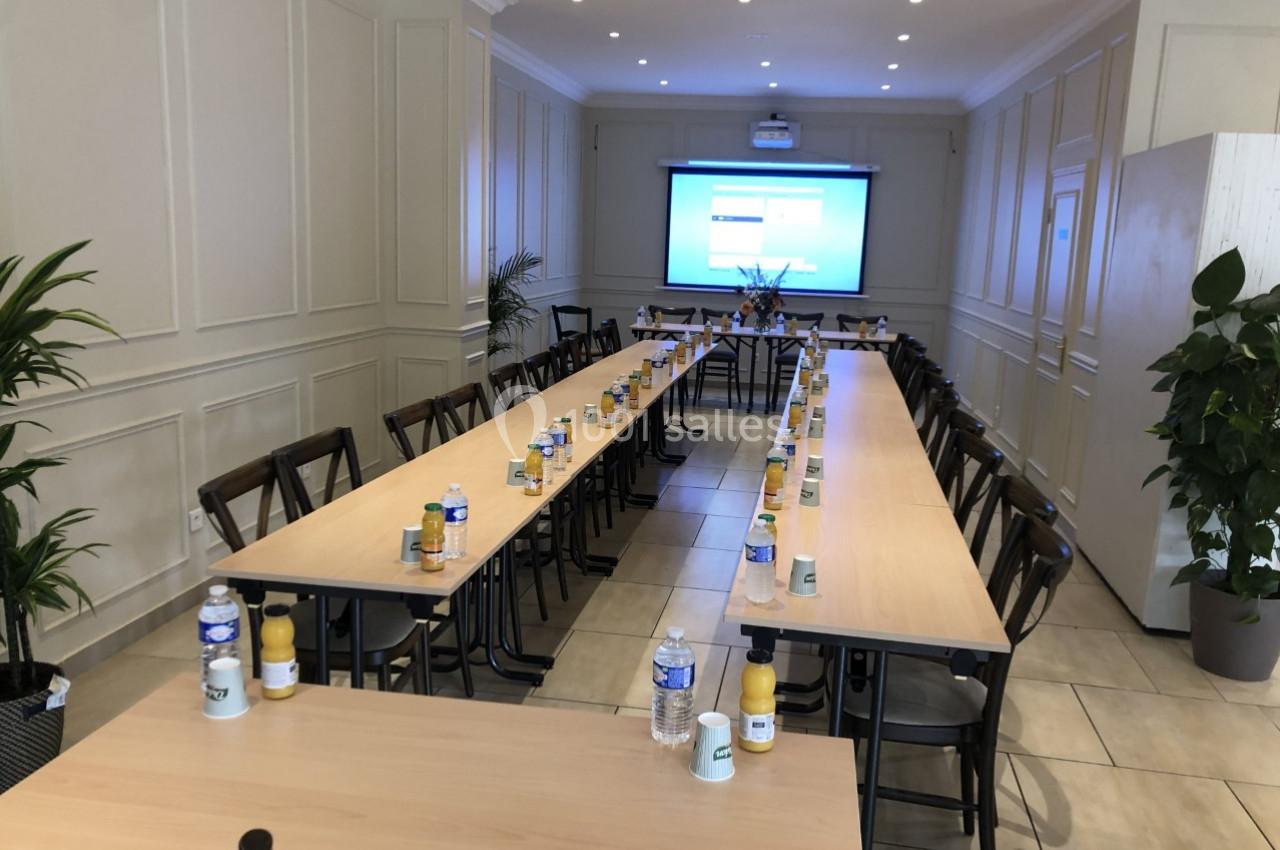 Salle de réunion lumineuse avec tables disposées en U, bouteilles d'eau et écran de projection allumé au fond.