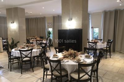 Salle décorée pour un événement, avec tables ornées de fleurs et colonnes blanches ajourées devant des rideaux beiges.