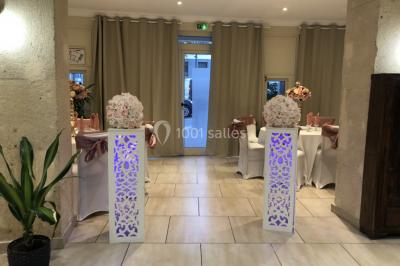 Salle décorée pour un événement, avec tables ornées de fleurs et colonnes blanches ajourées devant des rideaux beiges.