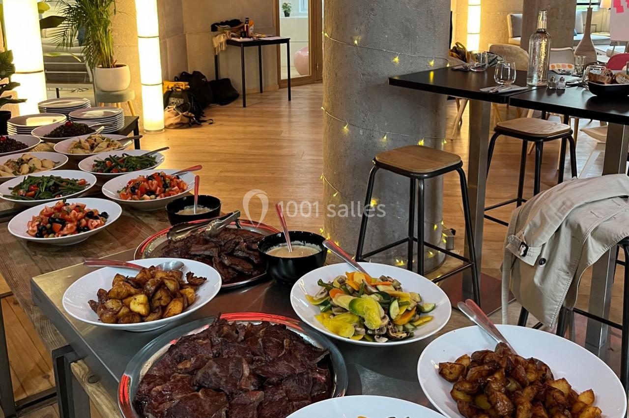Buffet varié avec plats de légumes, pommes de terre et viandes grillées, disposé dans une salle lumineuse.