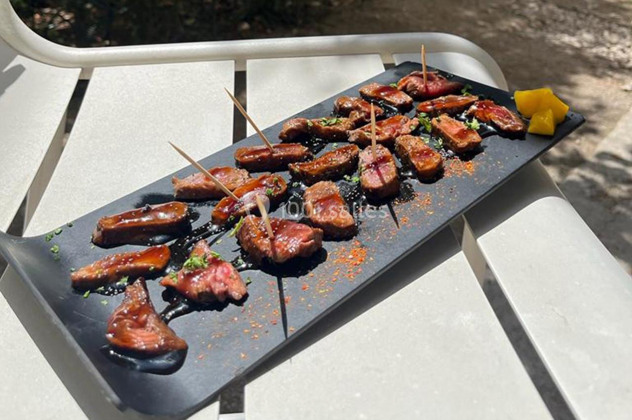 Assortiment de morceaux de viande grillée sur un plateau noir, présenté avec des brochettes et des épices.