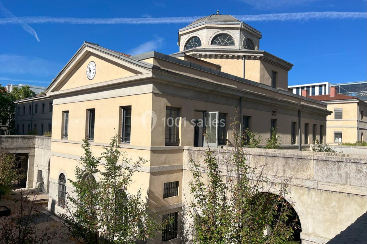 Bâtiment ancien avec façade beige, horloge centrale et dôme, entouré de végétation sous un ciel bleu.