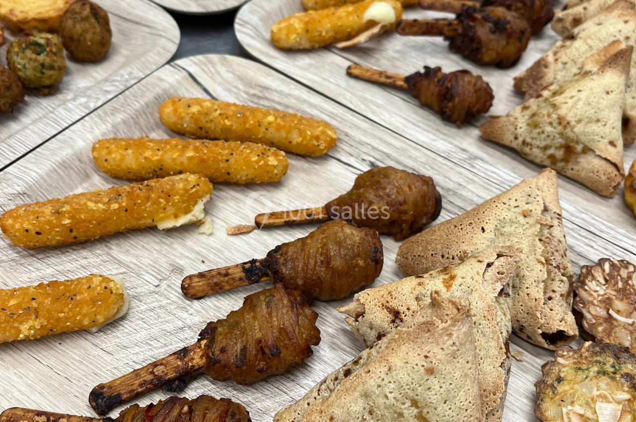 Assortiment de snacks salés variés, incluant samoussas, beignets et amuse-bouches, disposés sur des plateaux en bois.